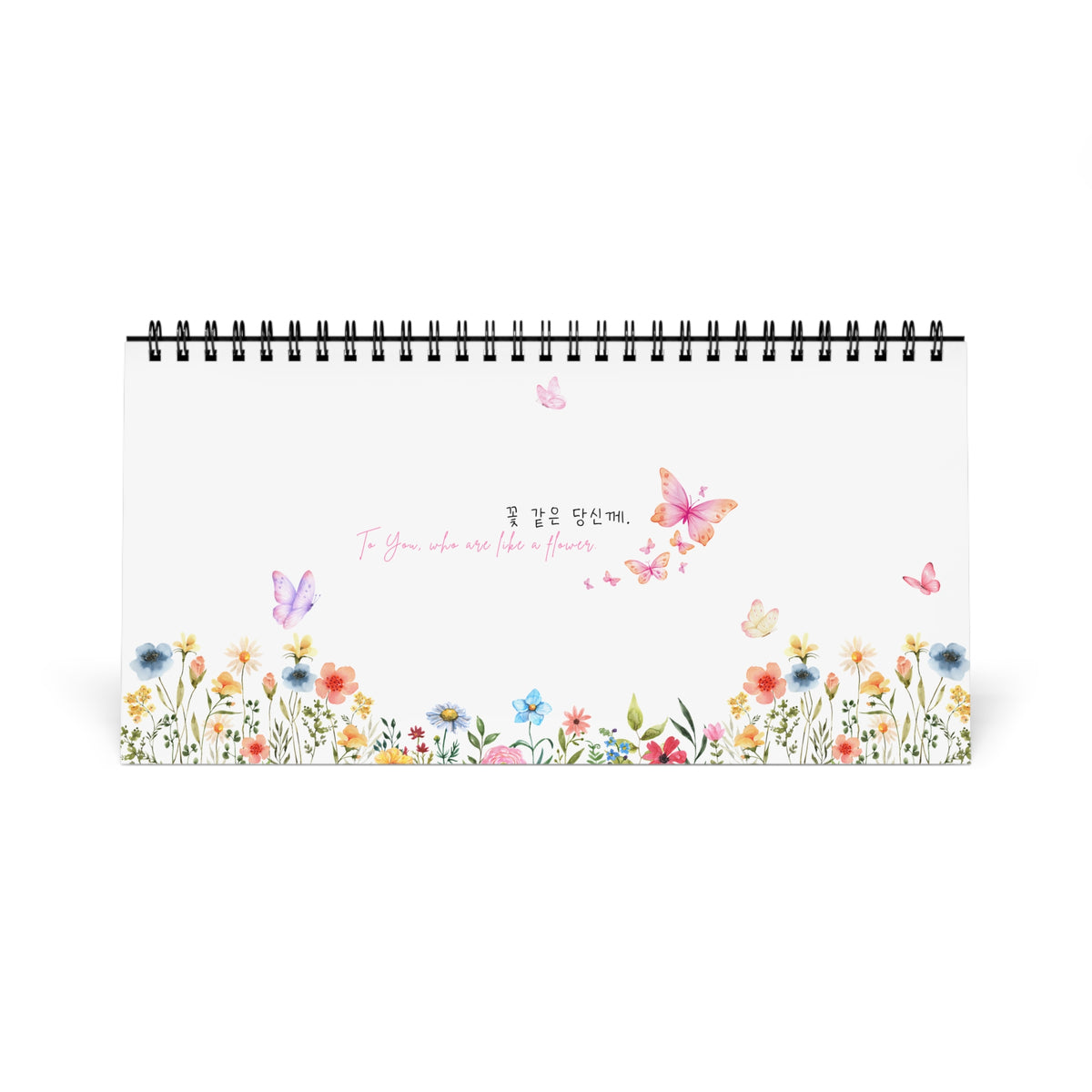 A spiral-bound desk calendar or notebook with a white cover, decorated with colorful watercolor flowers along the bottom border, butterflies, and the text 'To You, who is like a flowers.' in Korean (polite form) and English.